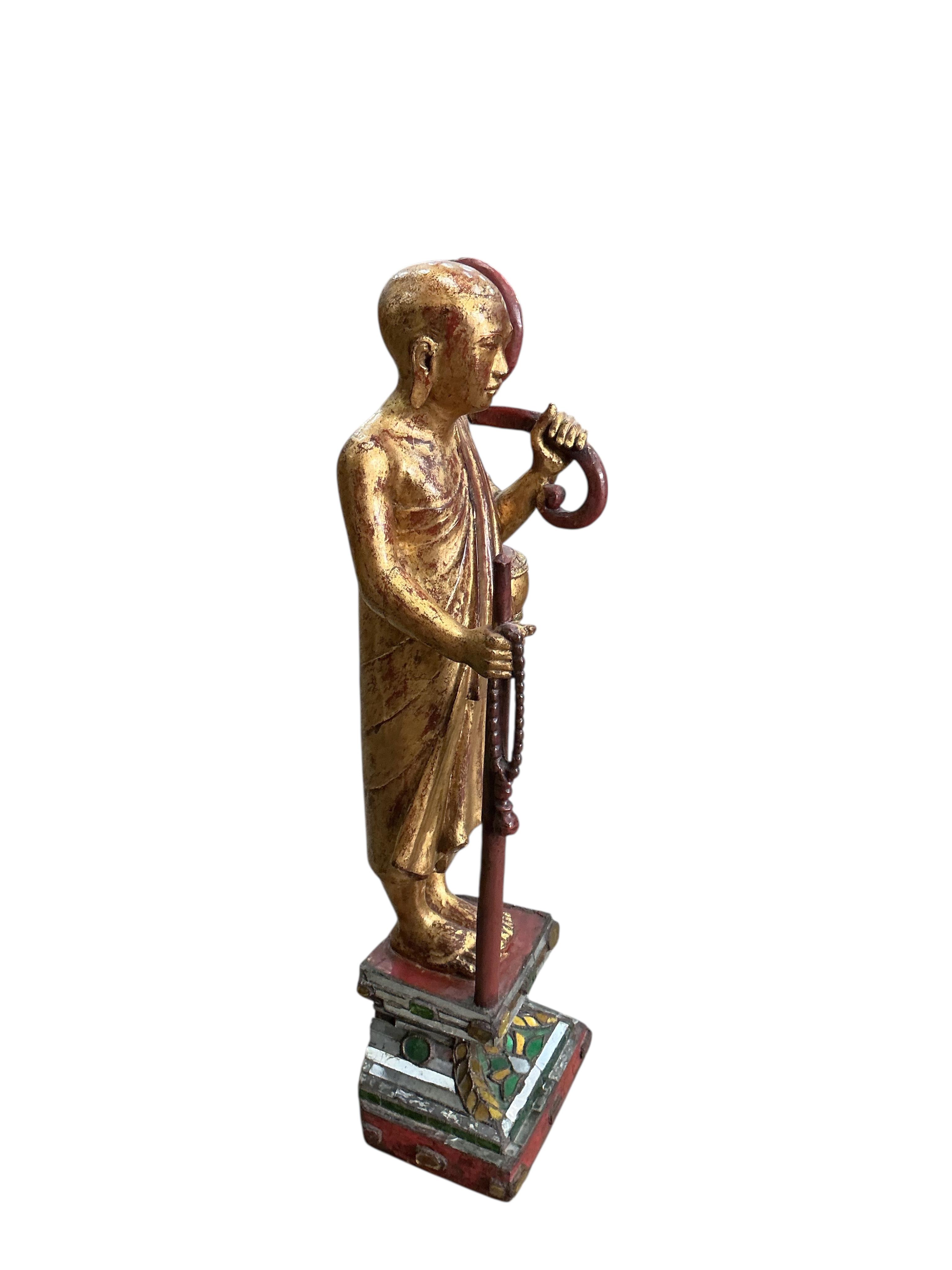 A Tibetan or Thai carved giltwood figure of a priest on a mirrored plinth, height 80cm